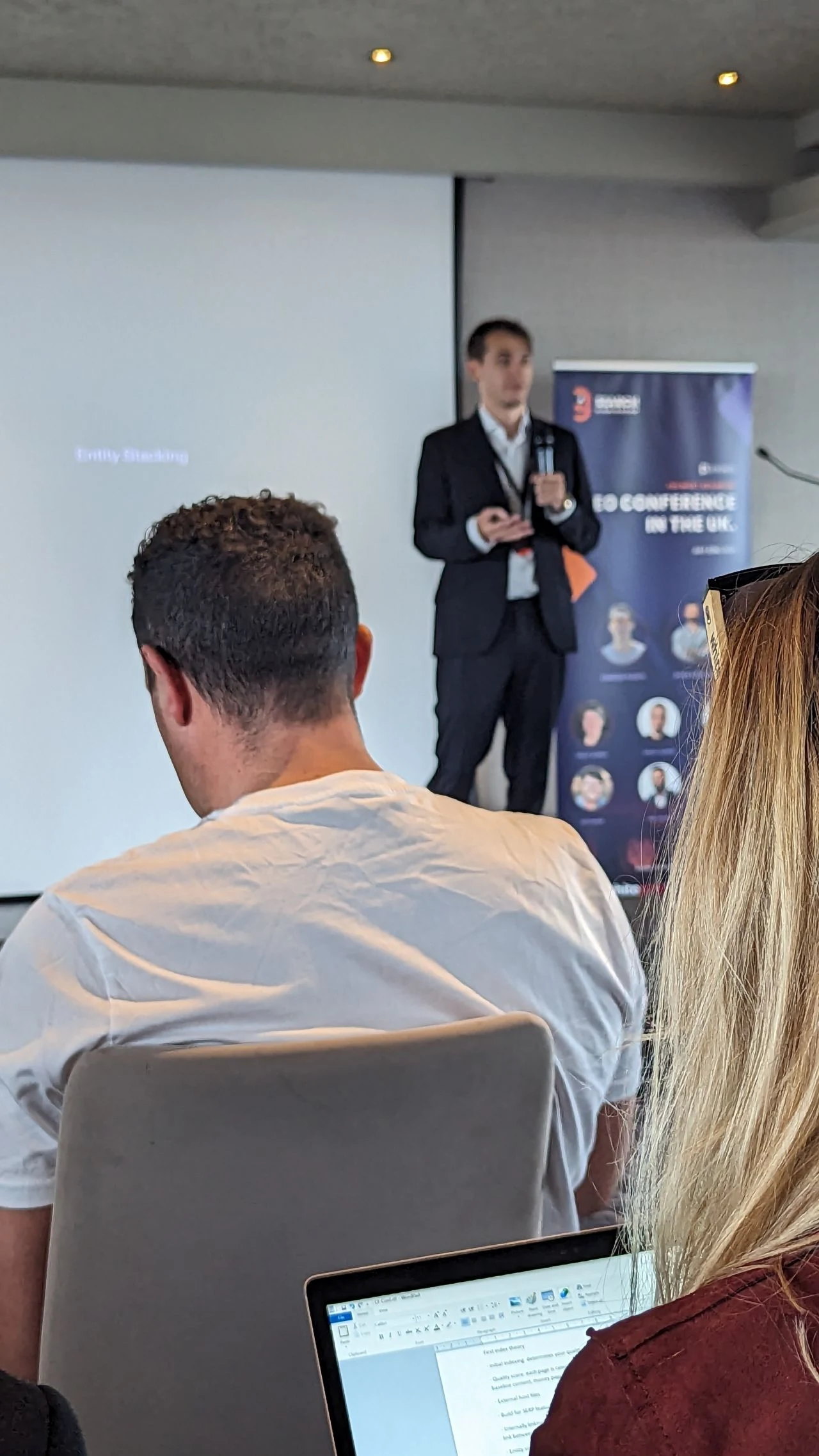 A speaker presenting an entity stacking session at Search Birmingham, the SEO conference in the UK, in front of the event banner